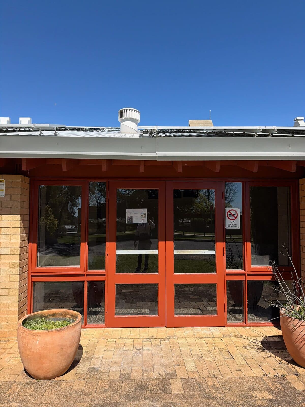 University campus entry with repainted orange red doors and exposed rafter ends above a paved forecourt, Orange NSW