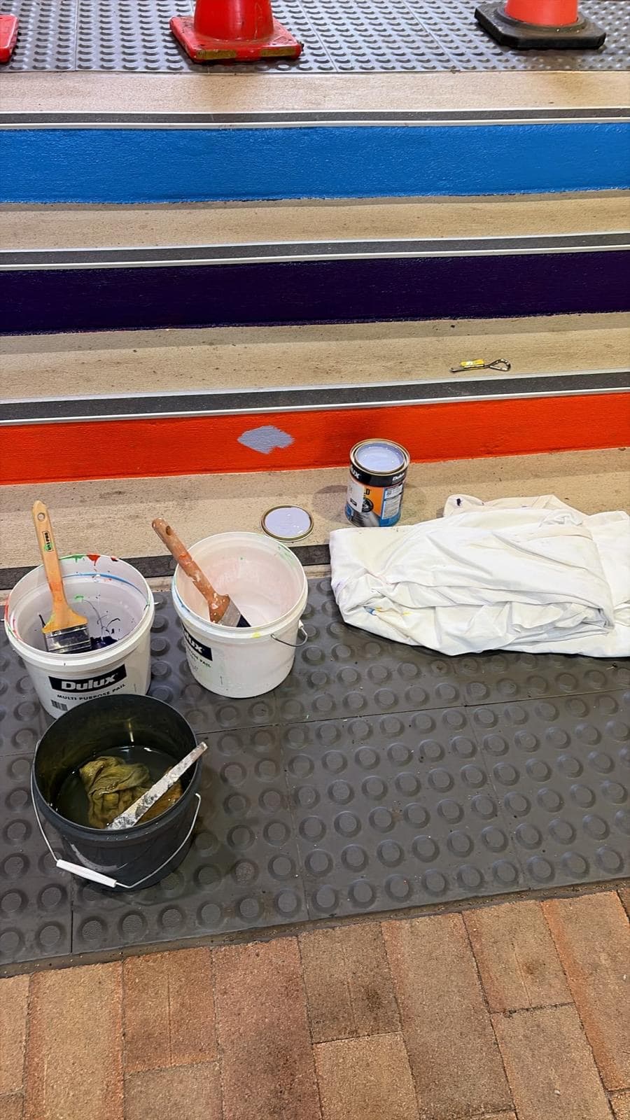 Dulux pails, brushes and a drop sheet beside part-painted stair nosings in blue, purple and orange at Charles Sturt University Orange
