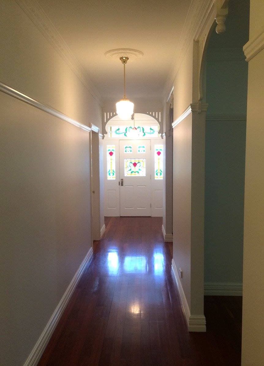 Freshly painted federation hallway with stained glass front door, white archway detail and polished timber floors