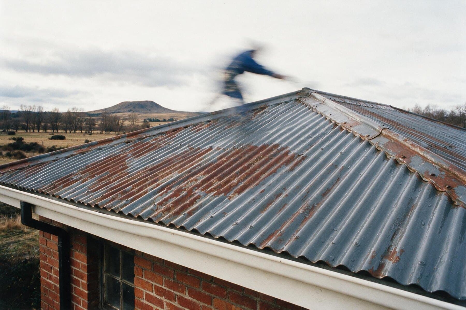 Corrugated steel roof on a red brick bungalow part way through a recoat, rust giving way to fresh grey, Central West NSW