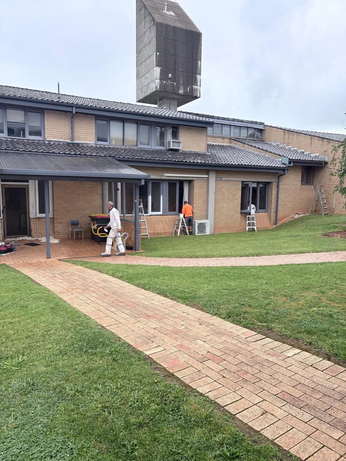 Brick path to a two storey campus building with painters at work on the window frames, Orange NSW