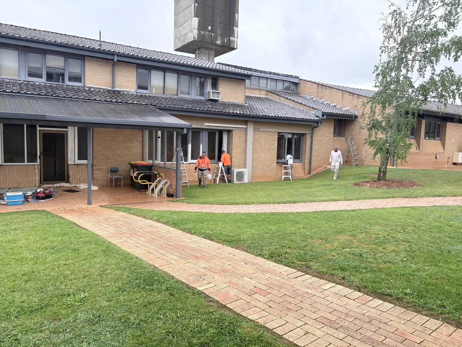 Window frame repaint under way along a cream brick campus building with tiled roofs, Orange NSW