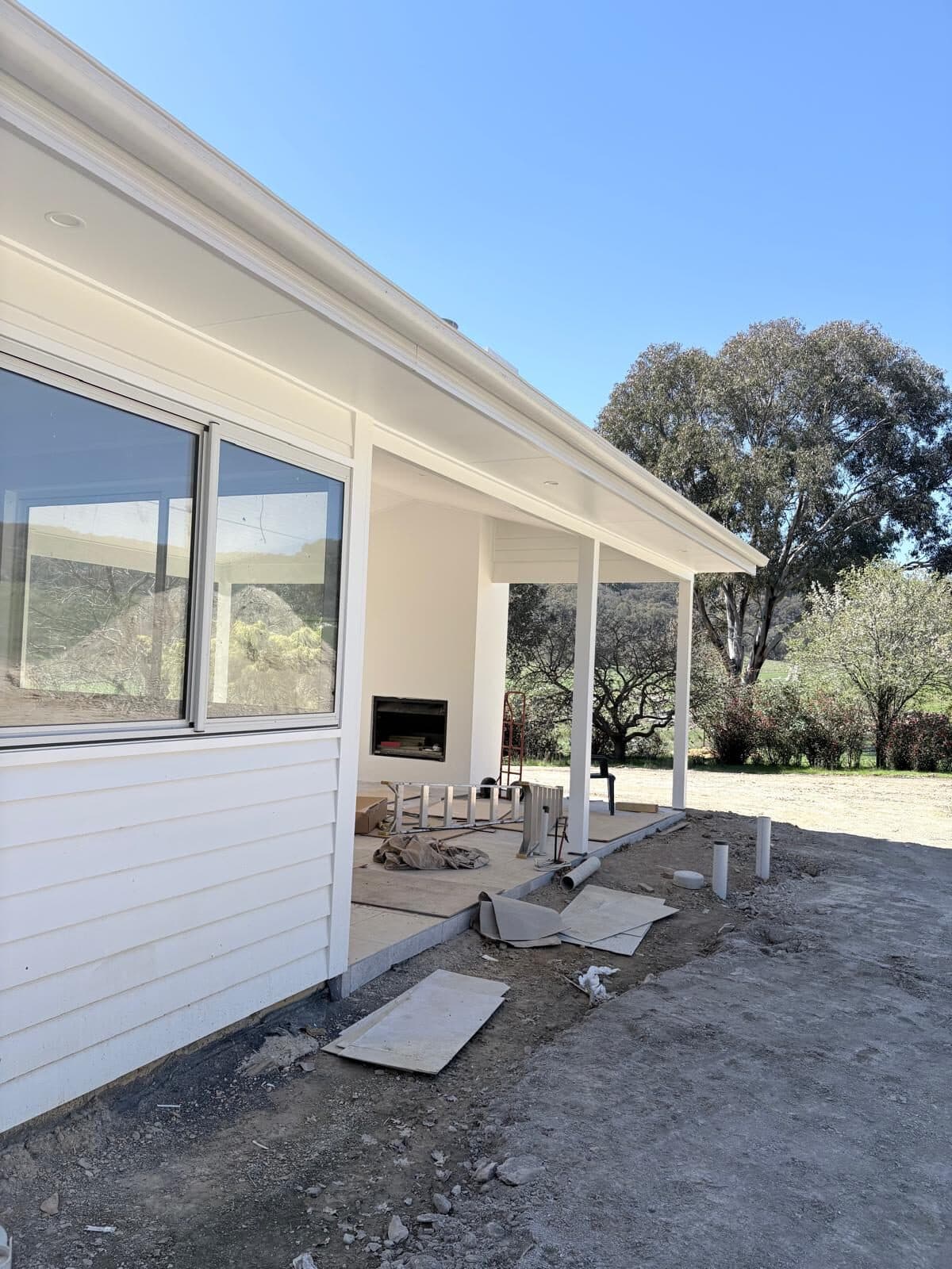 White weatherboard wall and verandah of a new wing with a window and covered walkway, rural setting