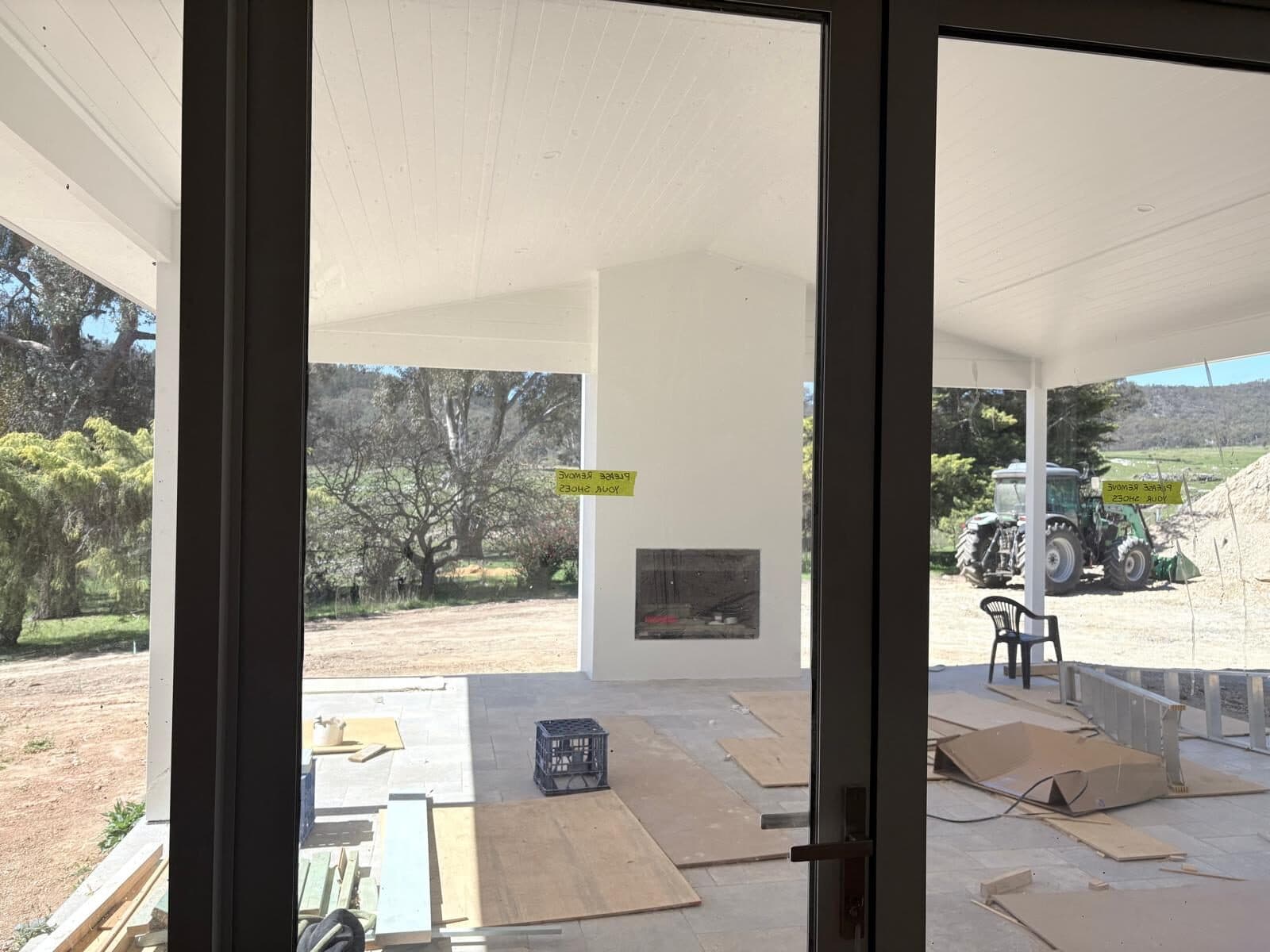 View through dark framed glass doors to a covered outdoor room with a fireplace, paddocks beyond