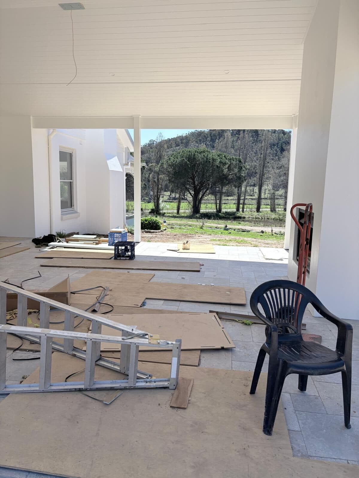 Covered outdoor room with a white lined ceiling under construction, materials stacked on the slab, rural outlook
