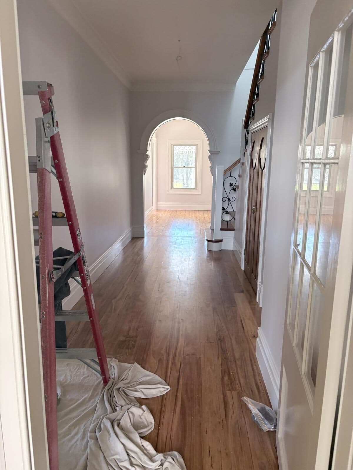 Hallway with a plastered arch and timber floor mid repaint, ladder and drop sheet in place