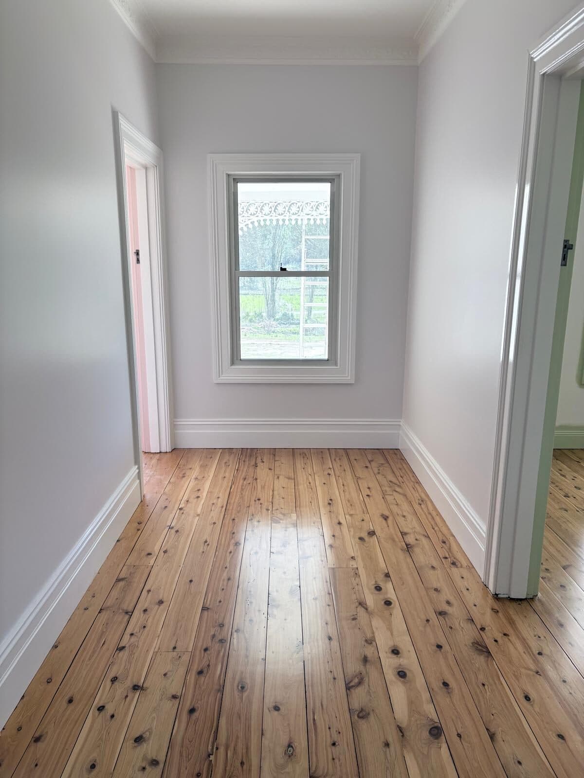 Hallway painted white with deep skirtings, a window to the paddocks and wide pine floorboards