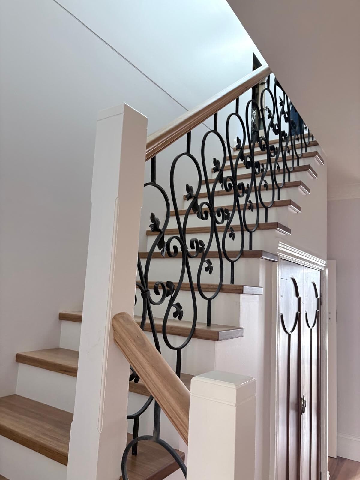 Timber staircase with a scrolled wrought iron balustrade and white painted stringer and walls in a rural homestead