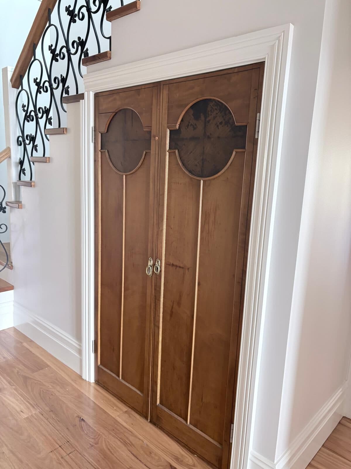 Timber double doors with arched glazing panels set into a white painted wall beneath a staircase