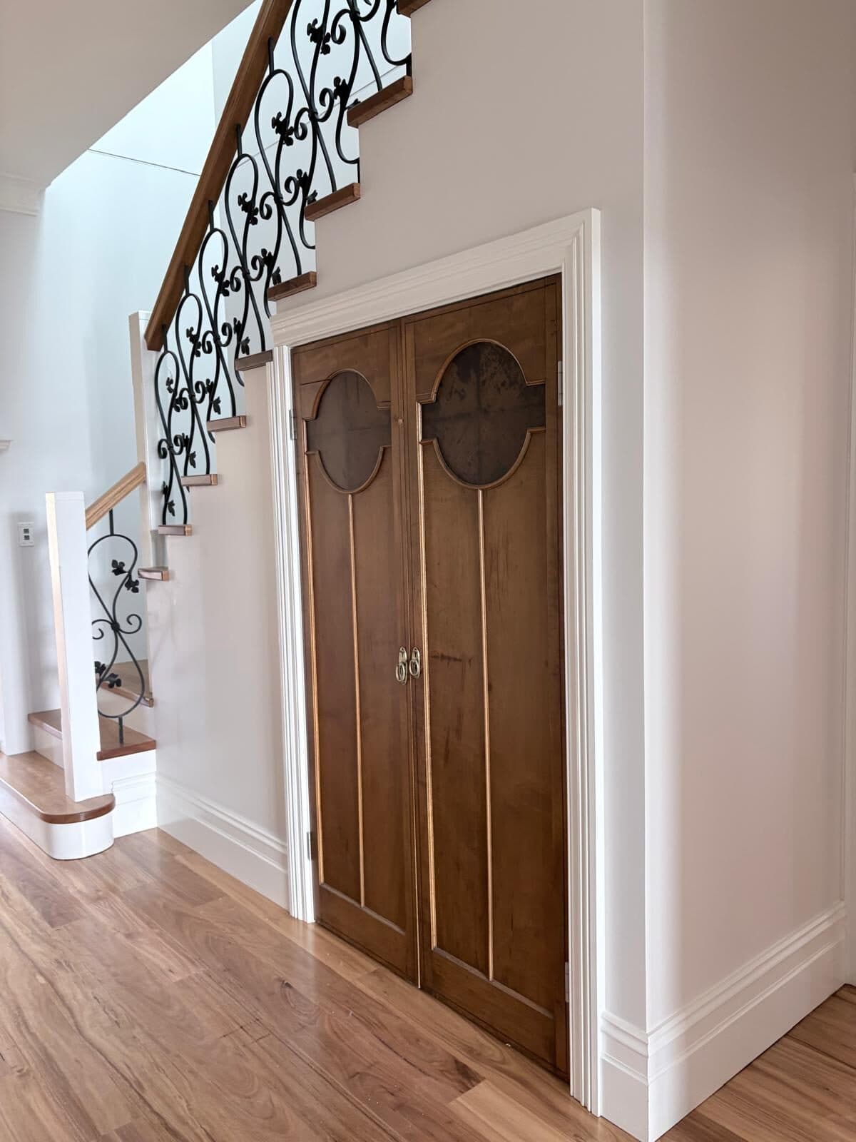Staircase with wrought iron balustrade beside timber double doors set into white painted walls