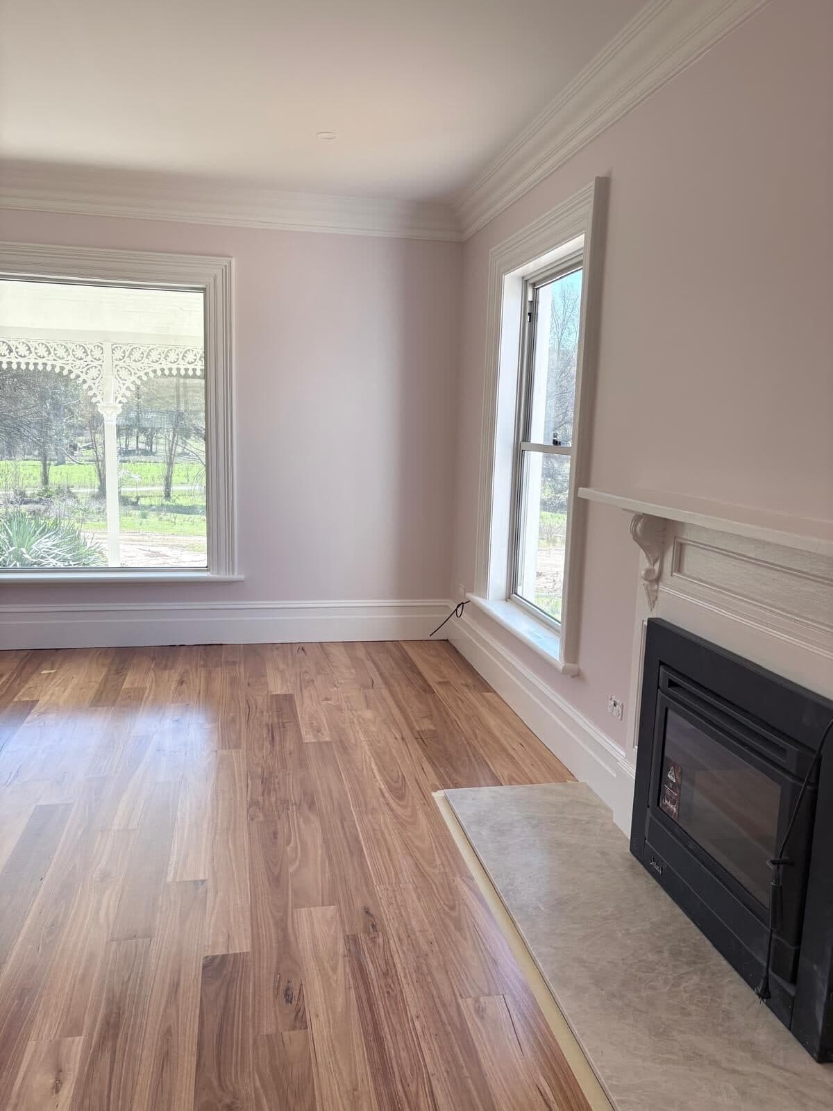Lounge room painted white with a black fireplace insert, timber mantel and two windows looking out to paddocks
