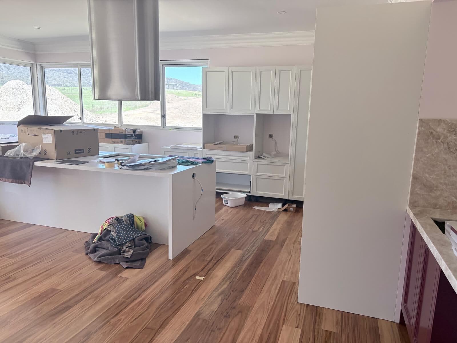 Kitchen with a large island bench, stainless rangehood and white cabinetry, windows framing a rural outlook