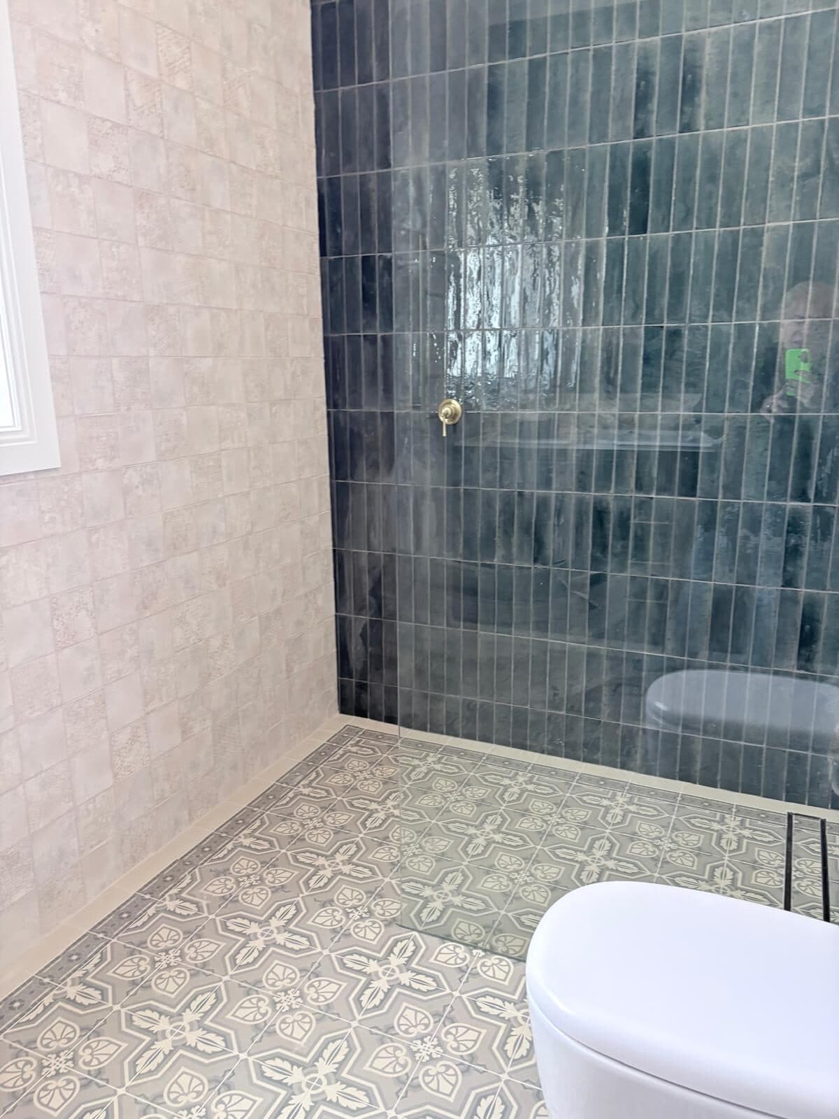 Bathroom with a freestanding bath, green glazed tiled shower and patterned floor tiles, walls painted in a soft neutral
