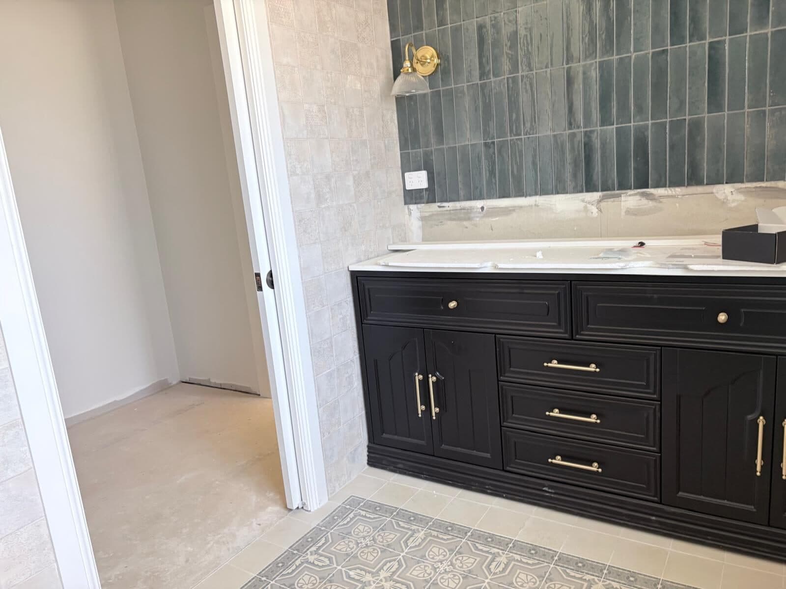 View from a doorway into a bathroom with a dark vanity, brass handles and a large mirror against green tile