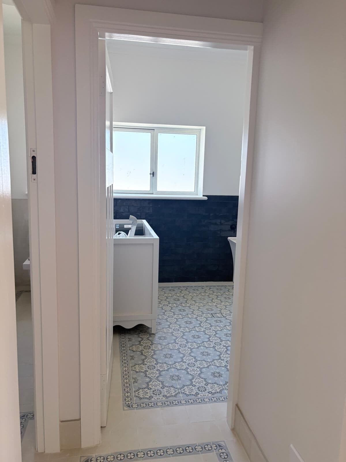 View through a white painted doorway into a laundry with navy cabinetry and patterned floor tiles