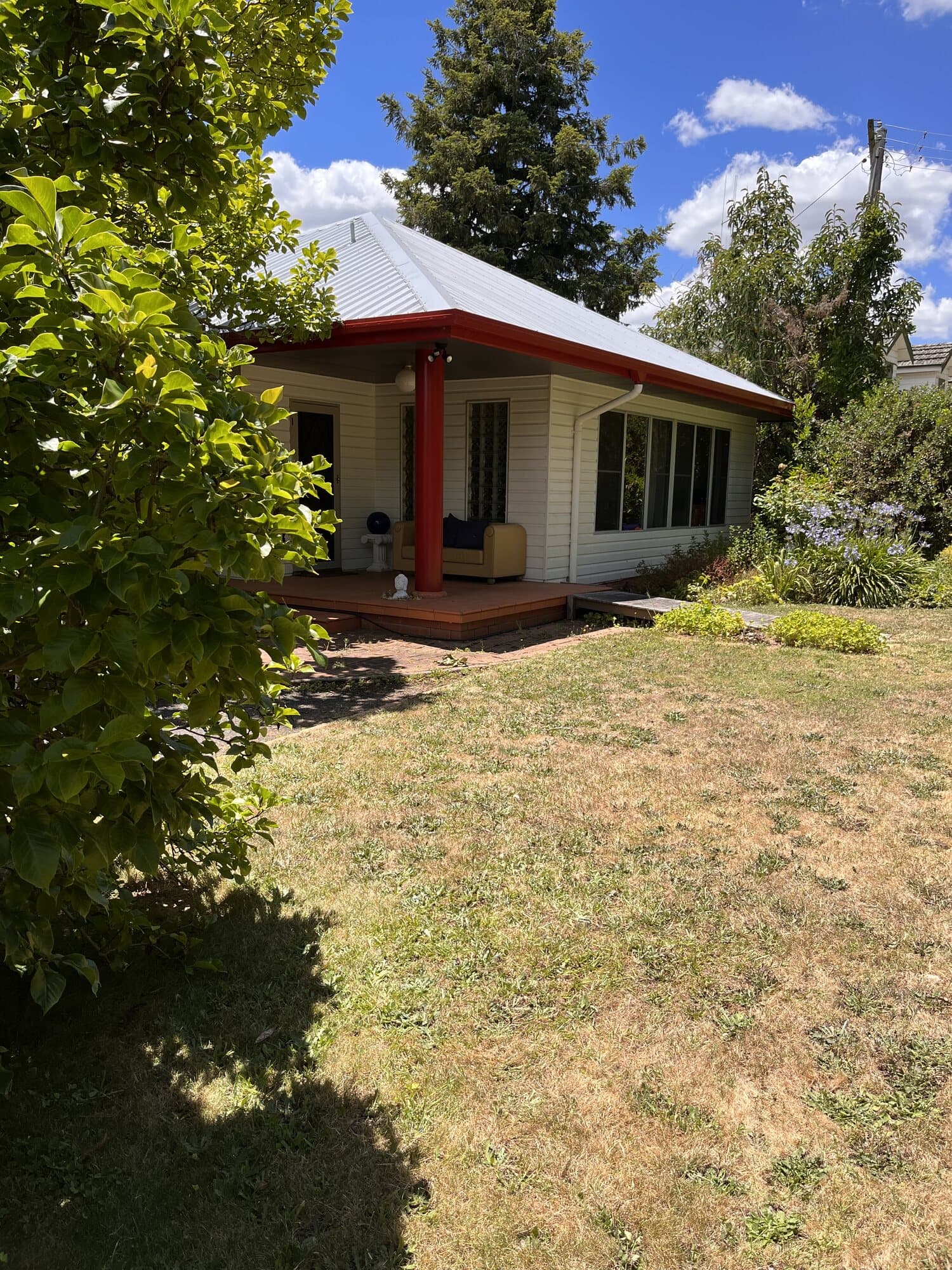 Corner of a cream weatherboard cottage with a recoated corrugated hip roof and red trim picked out along the fascia, Orange NSW