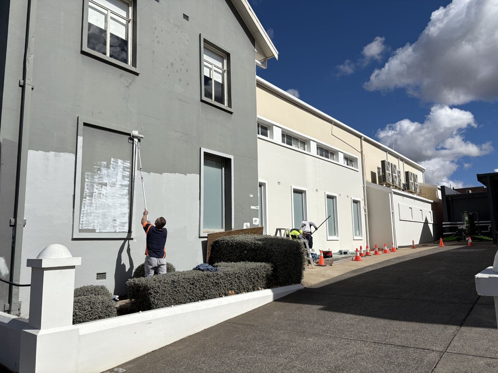 Two storey rendered commercial exterior being repainted in grey by Murrays Painting, patched render visible, Orange NSW