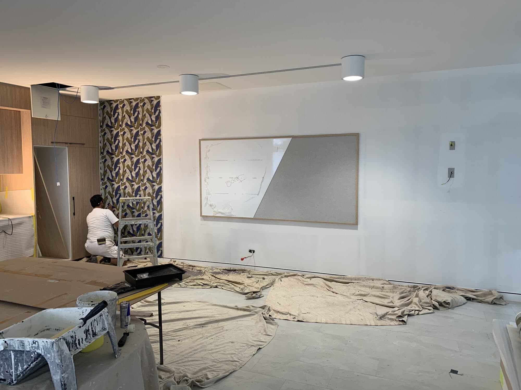 Painter hanging large scale botanical wallpaper onto a full height return during an interior fitout, Orange NSW